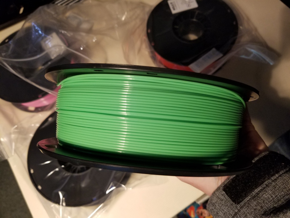 <EM><SMALL>Close-up photo of spool of green 3D printer filament being taken out of the box.</SMALL></EM>